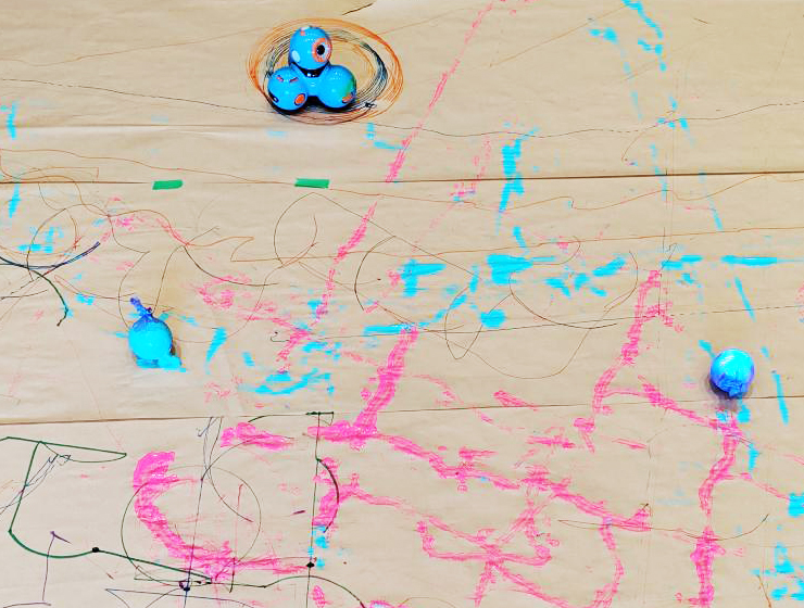 Three robots painting geometric shapes on the floor.